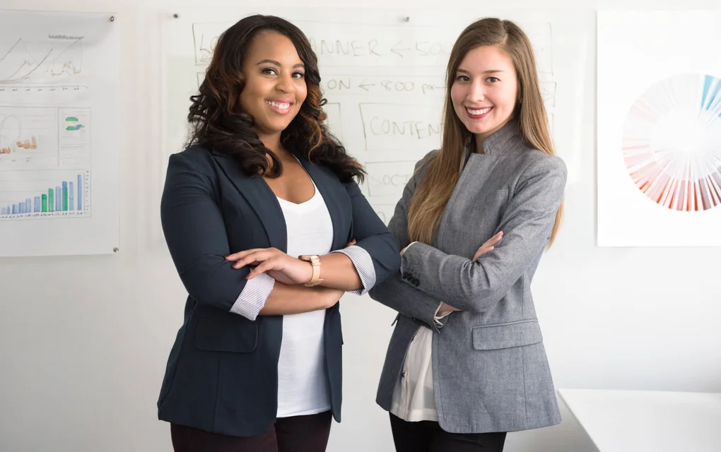 Two employees in a business setting with marketing charts and graphs displayed on the walls.