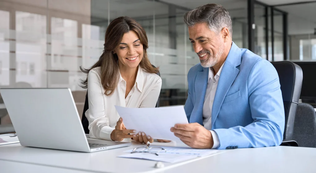 Staff work together in a business setting at a laptop.