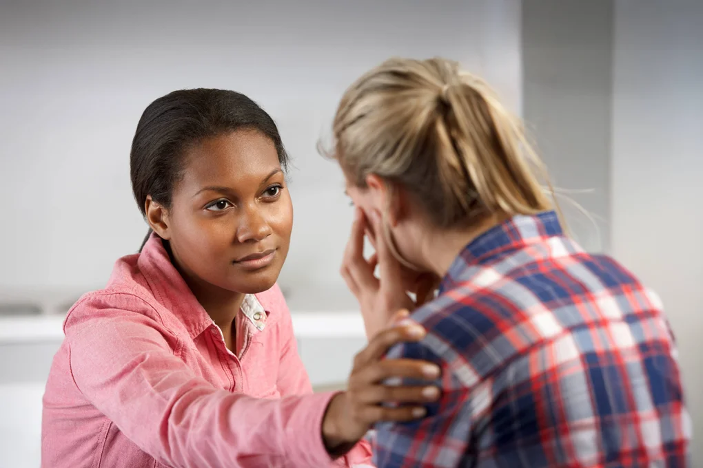A counselor looks attentively at a woman in distress. She reaches out to gently touch the patient's shoulder.