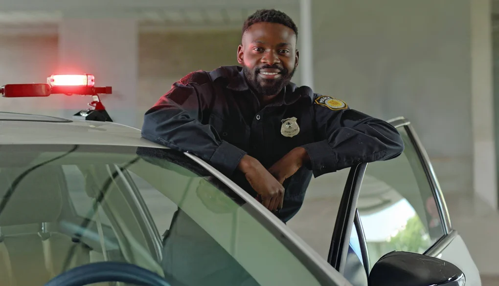 A police officer leans casually against the open door of his squad car, posing for a portrait.