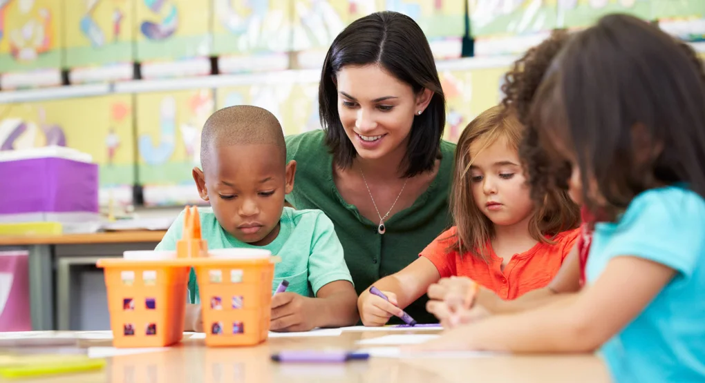 A teaching assistant helping 3 elementary students with an art project.