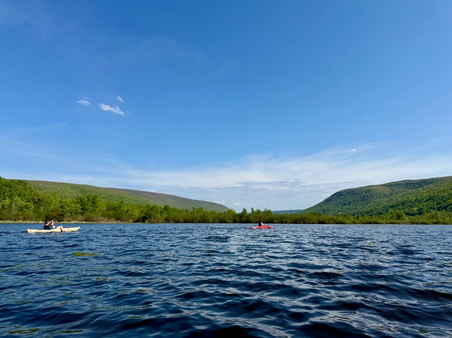 Two people kayaking on lake with green hillsides behind them.