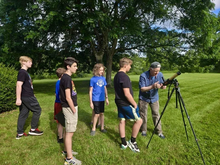 Young students in front of a tree in line to look through a telescope