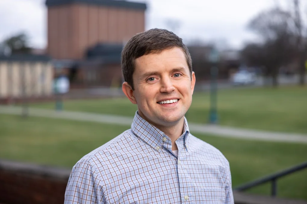 Head and shoulders photo of man in front of college building