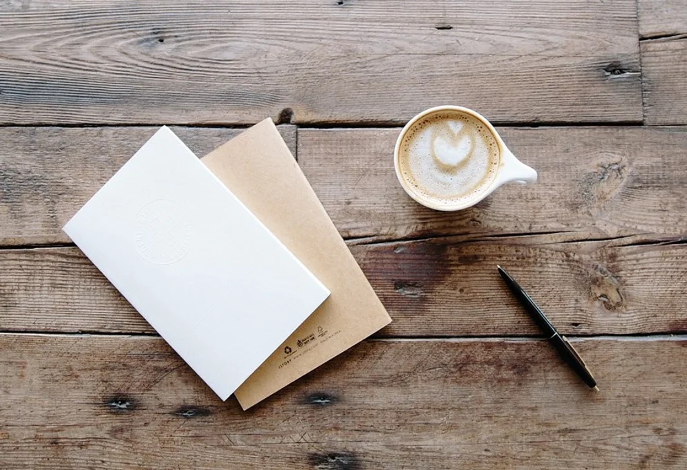 Photo of a notepad and latte on a wooden tabletop surface