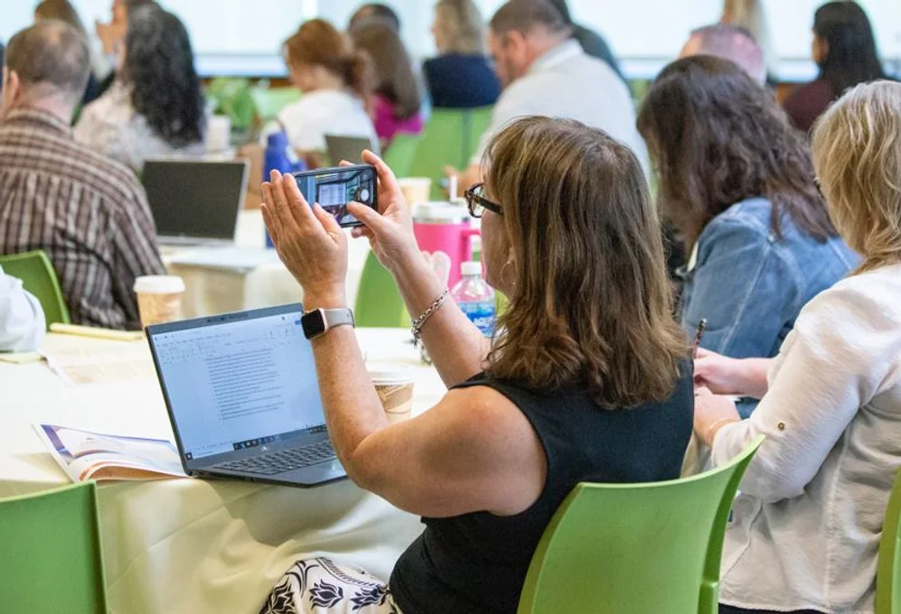 Woman at table with laptop taking photo with phone