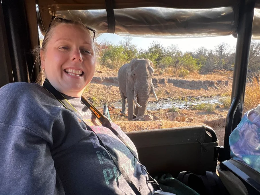 Woman in jeep smiling with elephant in background