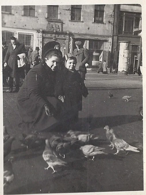 A woman bends down to feed birds with her toddler son in 1950s Wroclaw, Poland