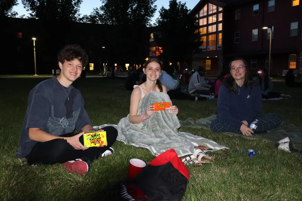 Three students sitting outside for an outdoor movie screening.