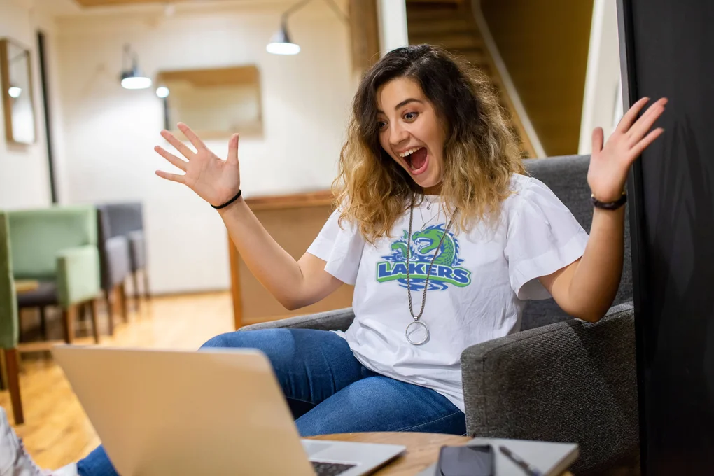 A girl wearing an FLCC lakers t-shirt looking at a laptop in excitement