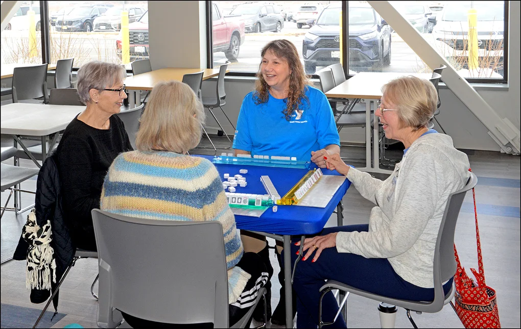 Four women, a YMCA staff member, and 3 senior citizens sitting around a table playing a game