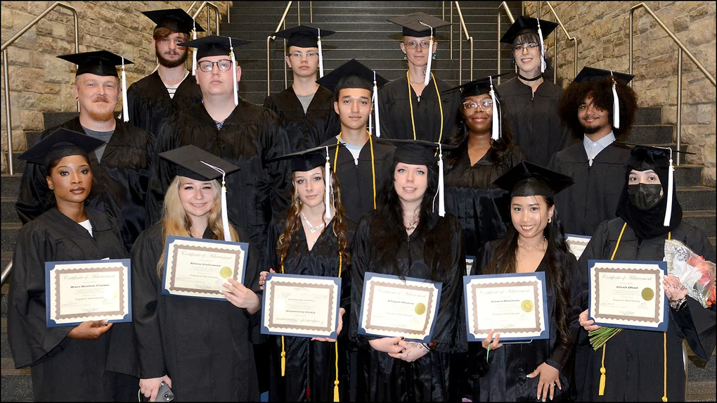 15 graduates in black caps and gowns posing on stairs