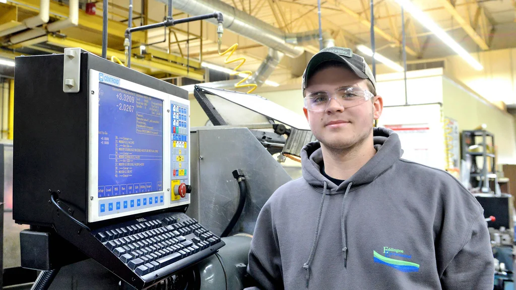 A manufacturing machinist student in front of several pieces of equipment.