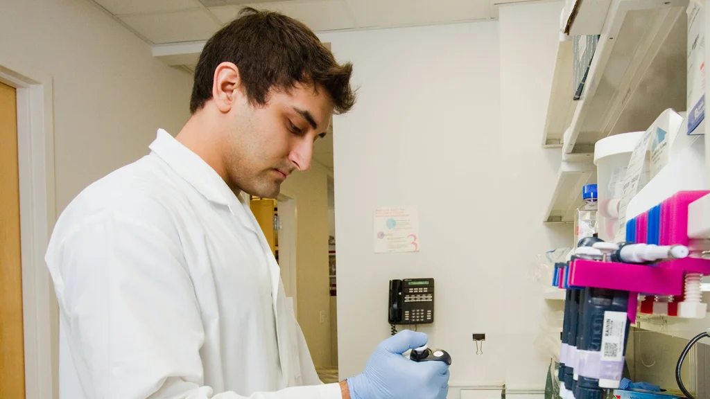 A career training participant in medical lab coat pouring liquid into vials.