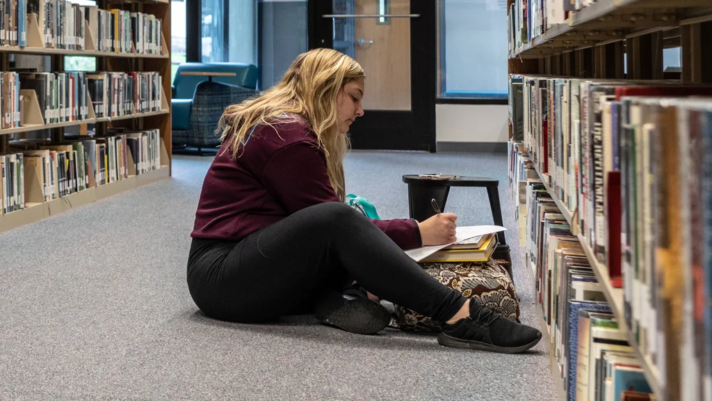 FLCC student chooses a library book from the reference section at the Canandaigua campus.