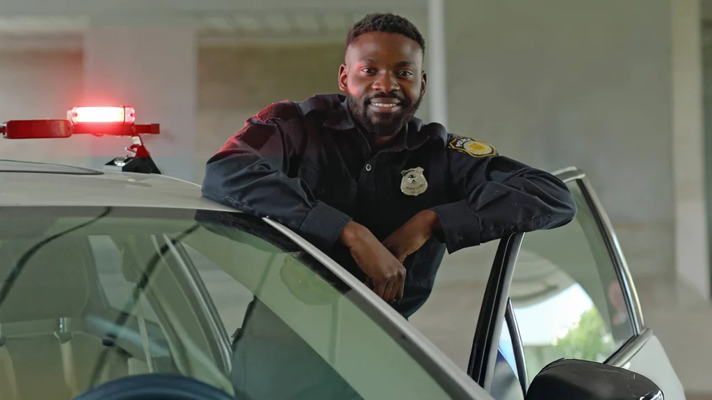 A police officer leans casually against the open door of his squad car, posing for a portrait.