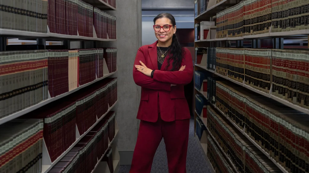 FLCC paralegal student standing in the Library among legal books.
