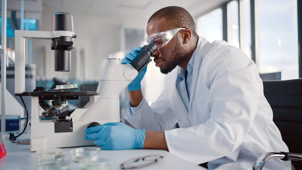 Lab tech looks at a slide through a microscope in the workplace.
