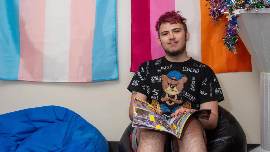 An FLCC student sits in front of a row of pride flags hanging on the wall.