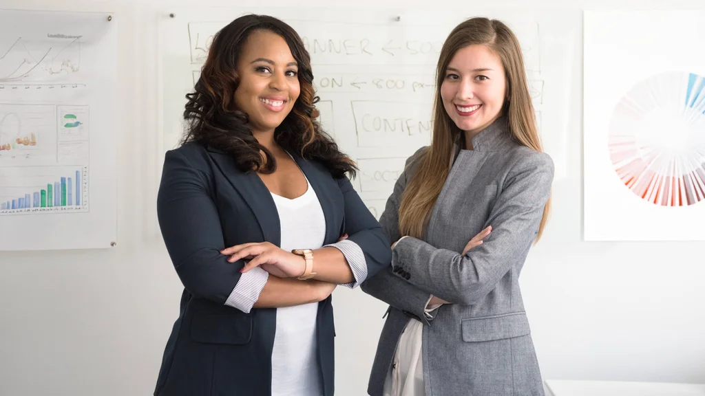 Two employees in a business setting with marketing charts and graphs displayed on the walls.