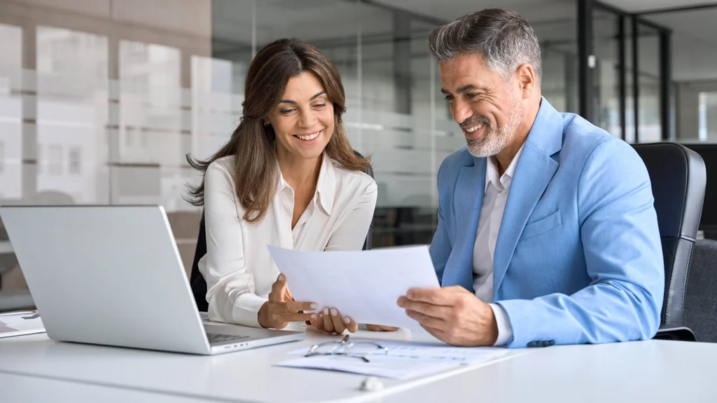 Staff work together in a business setting at a laptop.