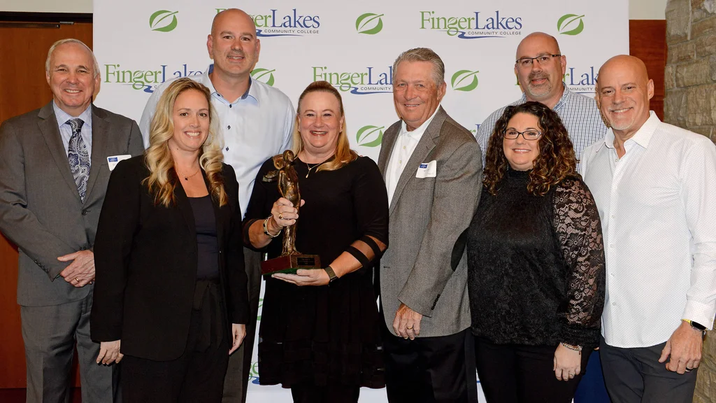 Distinguished Alumni Award winner with trophy in hand stands with FLCC staff.
