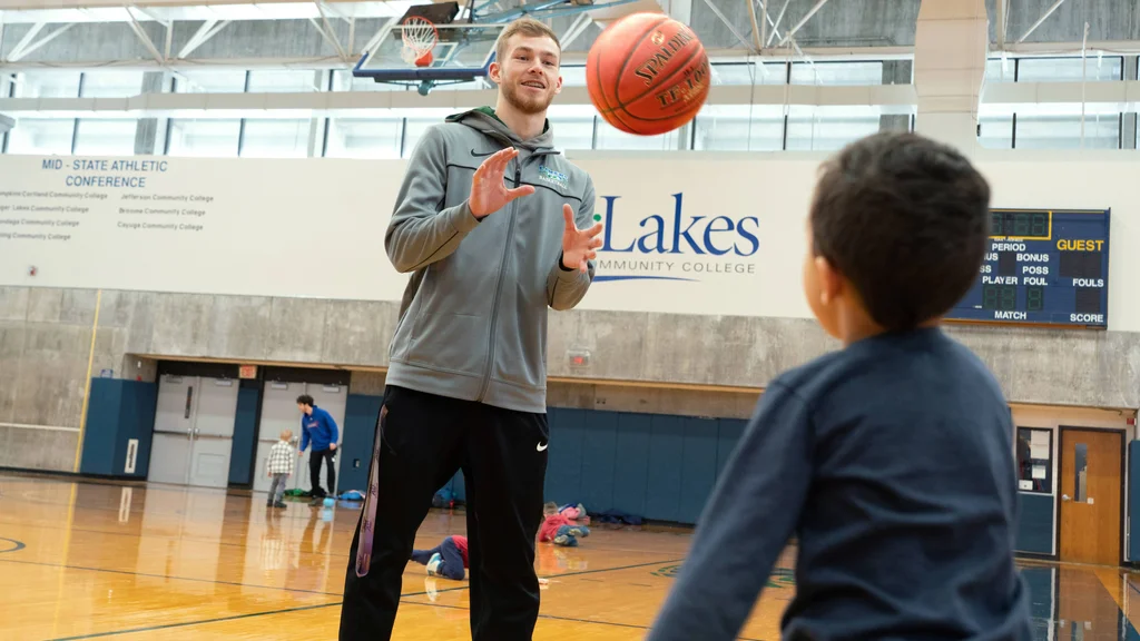 A Physical Education and Exercise Science student tossing a basketball with a grade-school student in the FLCC gymnasium