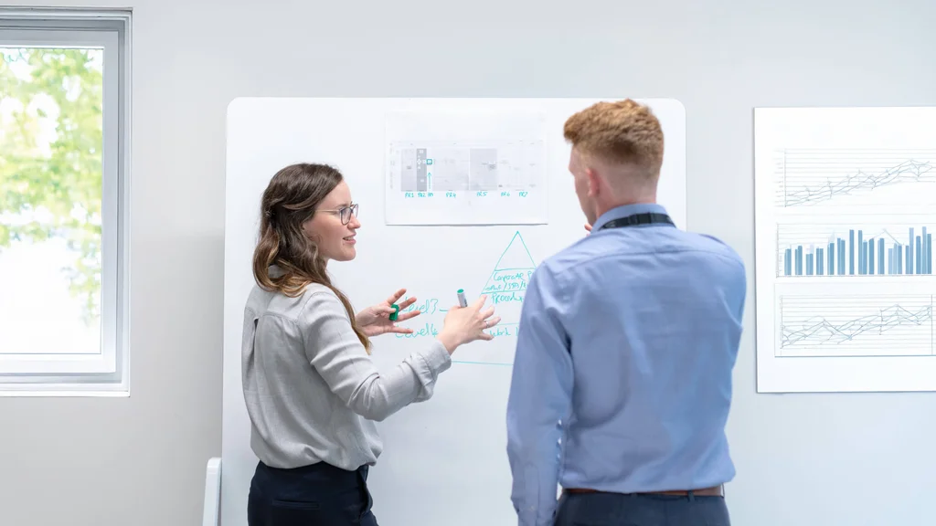 Two people holding an active brainstorming session and drawing on a whiteboard.