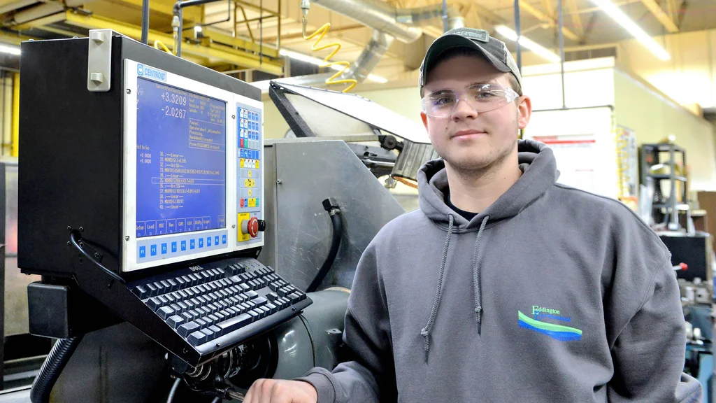 A manufacturing machinist student in front of several pieces of equipment.