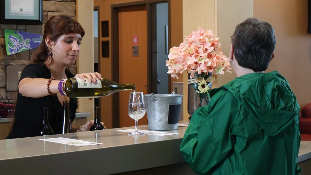 A woman serves a glass of wine to an event attendee.