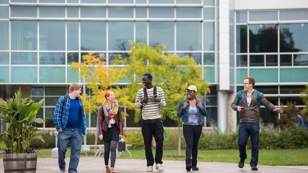 Five students walk in a group outside of FLCC main campus, talking and laughing.