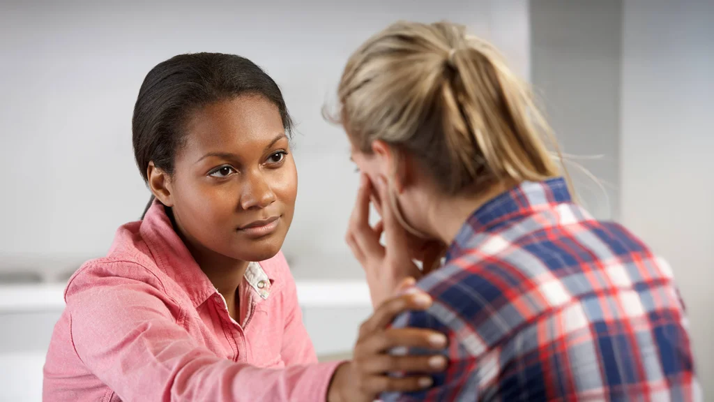 A counselor looks attentively at a woman in distress. She reaches out to gently touch the patient's shoulder.