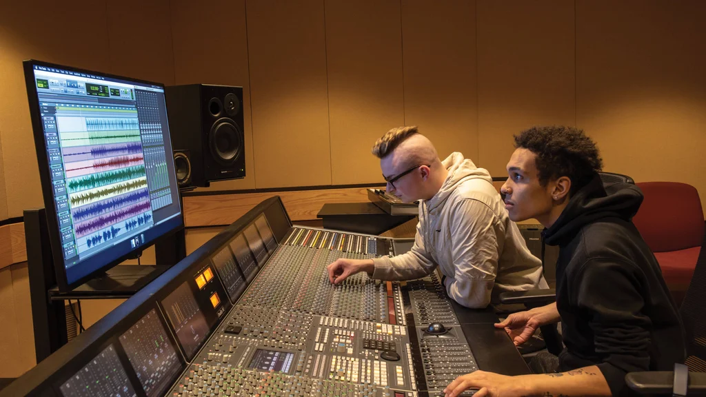 Two music recording technology students adjusting setting on a professional studio soundboard.