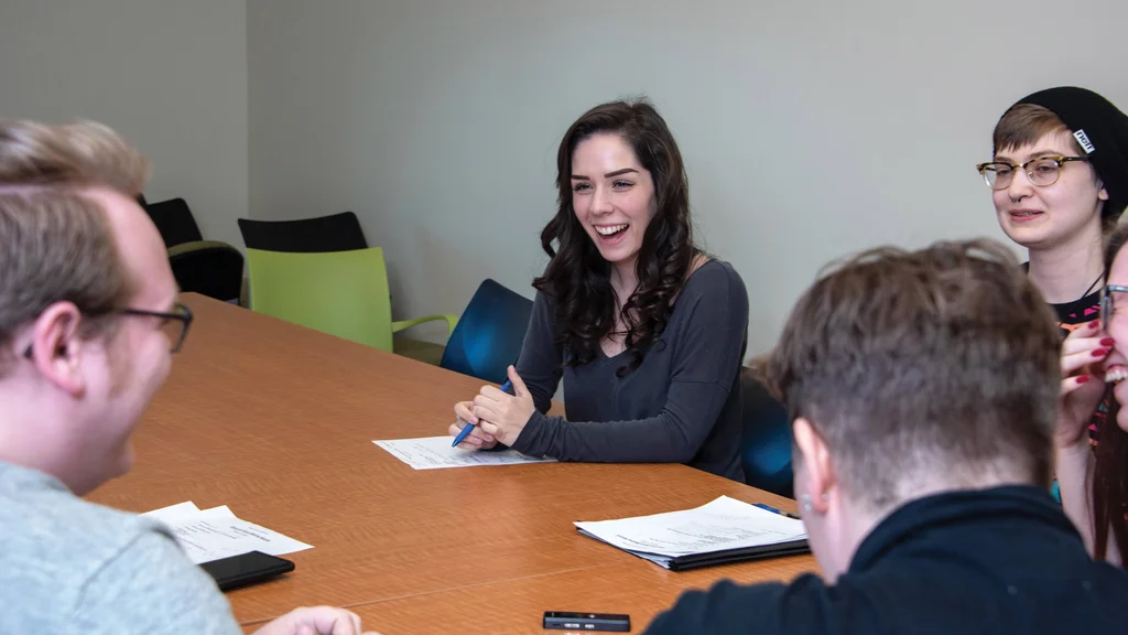 An FLCC student sitting behind a long conference table, sharing a laugh with two others in the room.