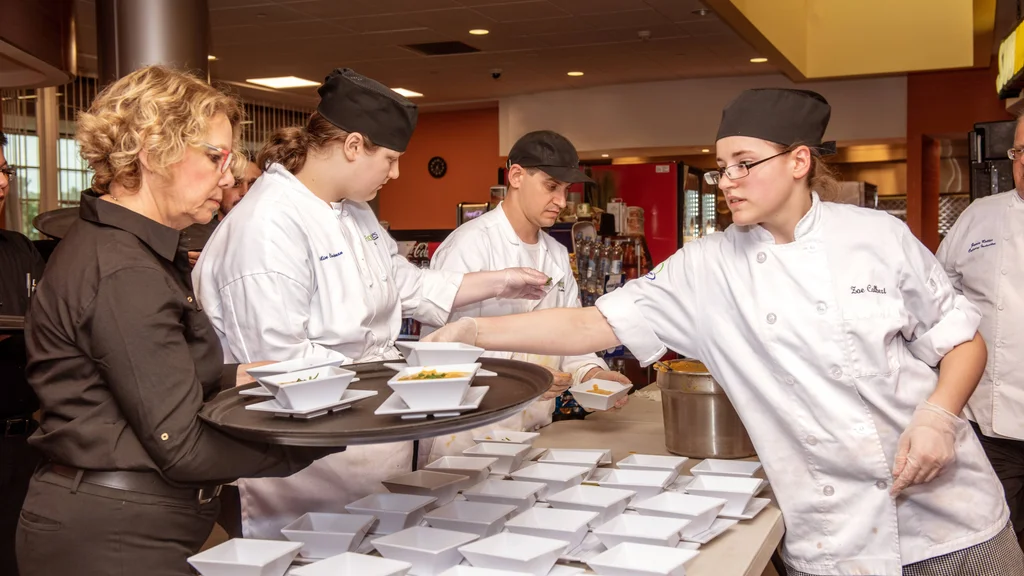 A group of Culinary Arts students in white chef's jackets dishing up soup for an event.