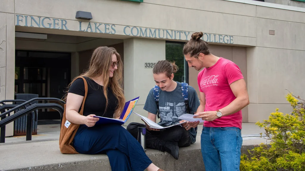 Three students study outside and work together on schoolwork near the entrance of the FLCC main campus.