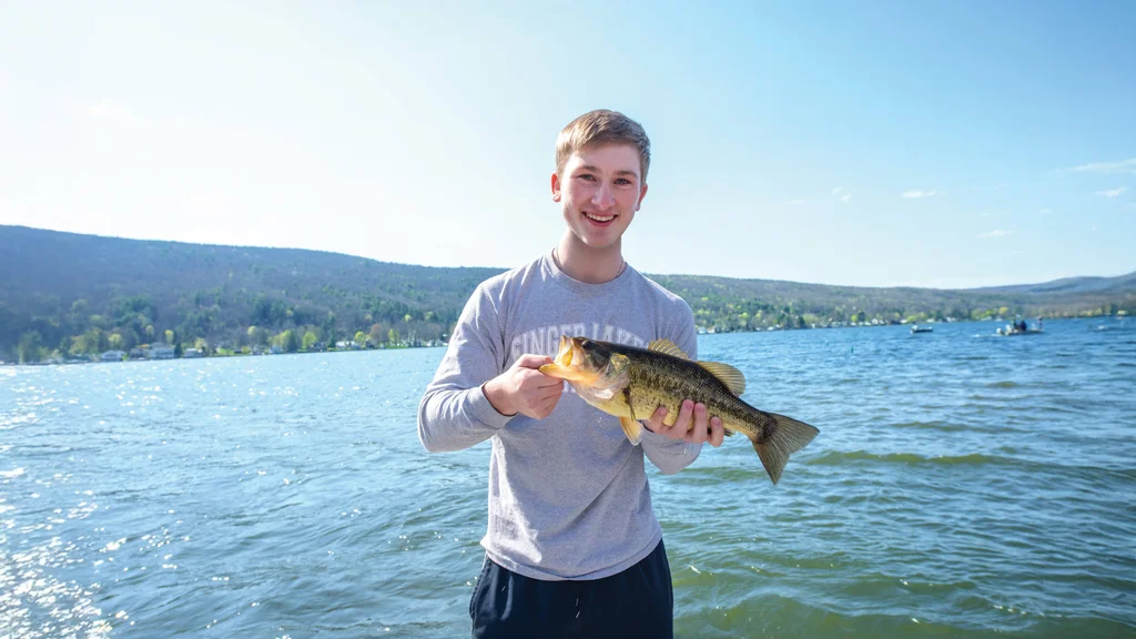 A student holding a fish captured during an FLCC field experience on Canandaigua Lake.