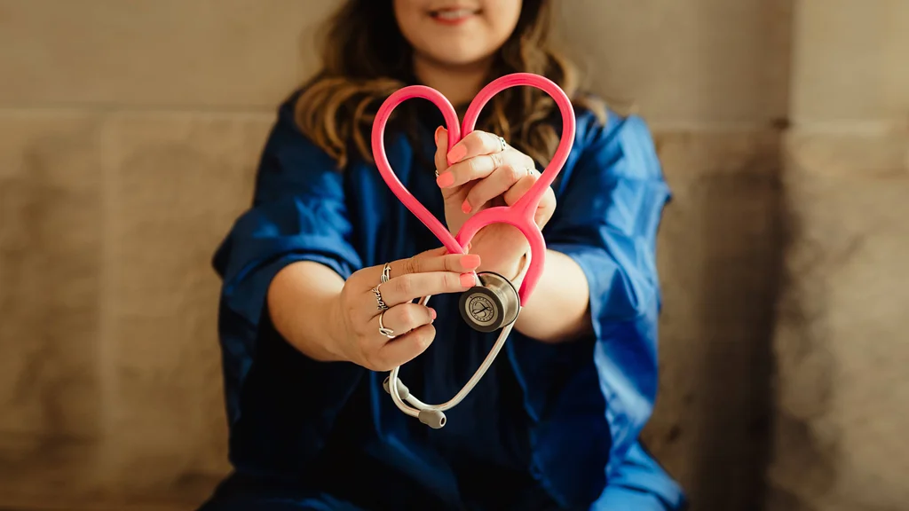 A medical professional holding a stethoscope in the shape of a heart.