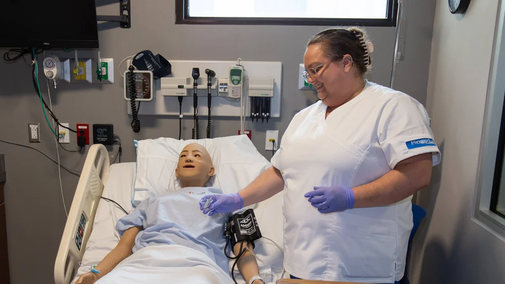 FLCC CNA student learning in a nursing simulation bay.
