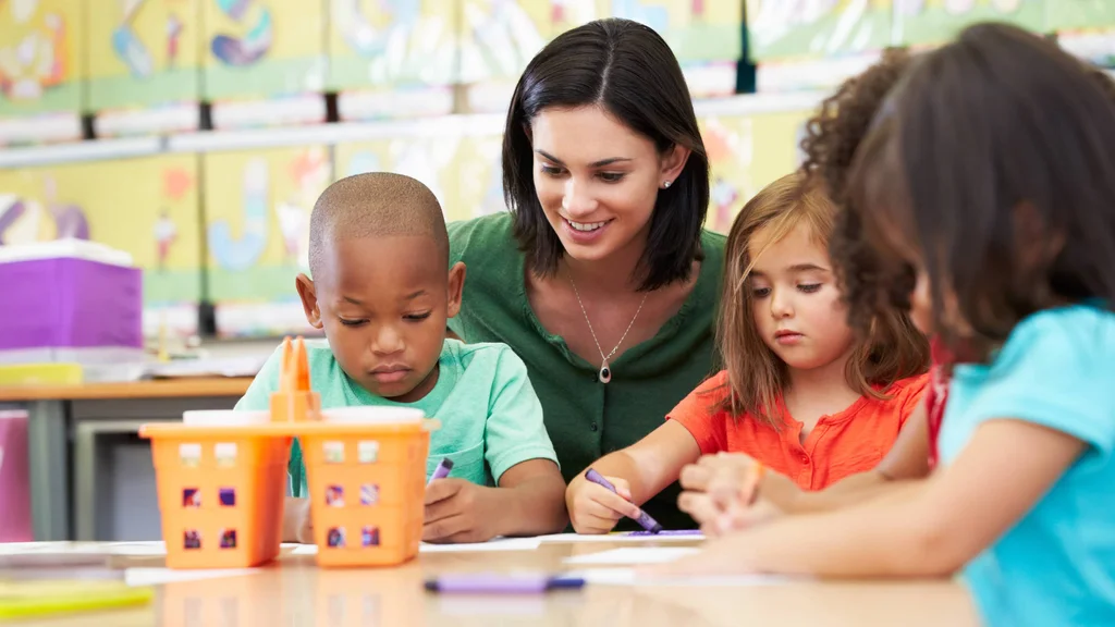 A teaching assistant helping 3 elementary students with an art project.