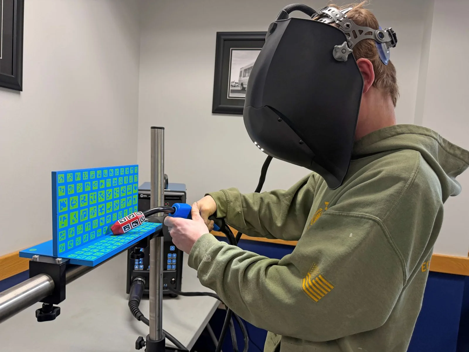 An instructor stands next to a man in a welding helmet using computer simulation technology