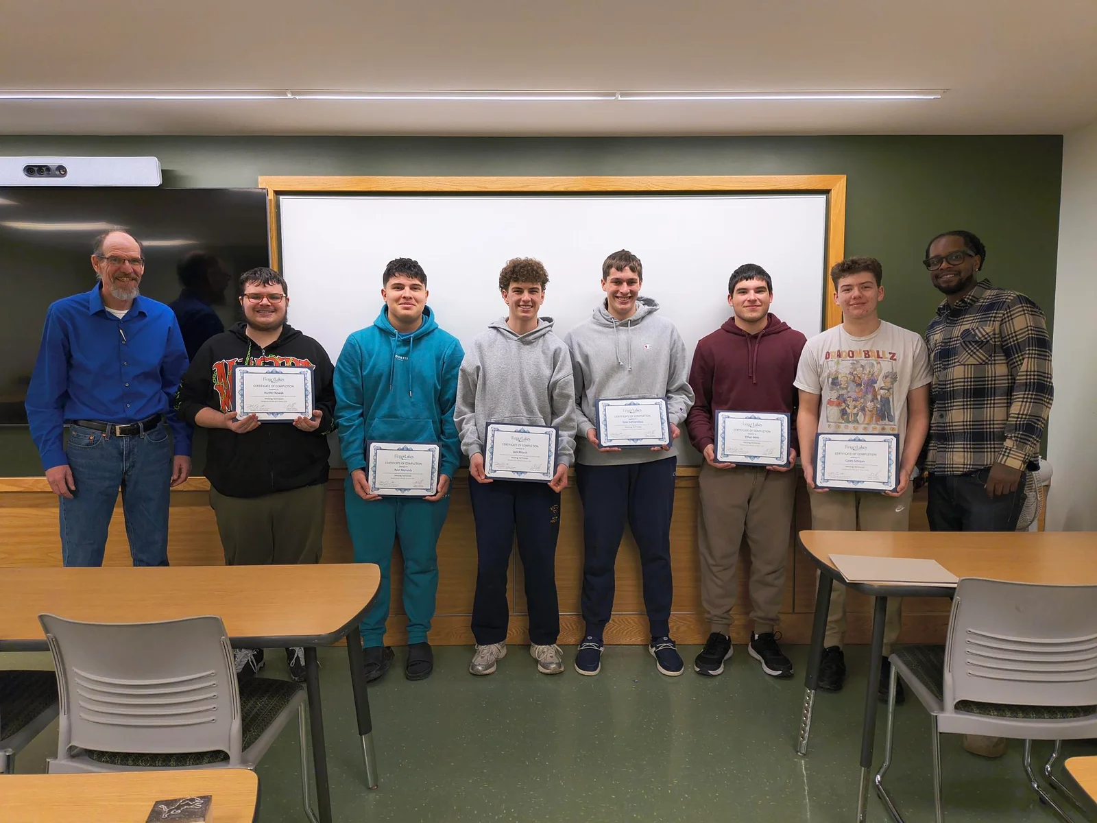 An instructor stands next to a man in a welding helmet using computer simulation technology