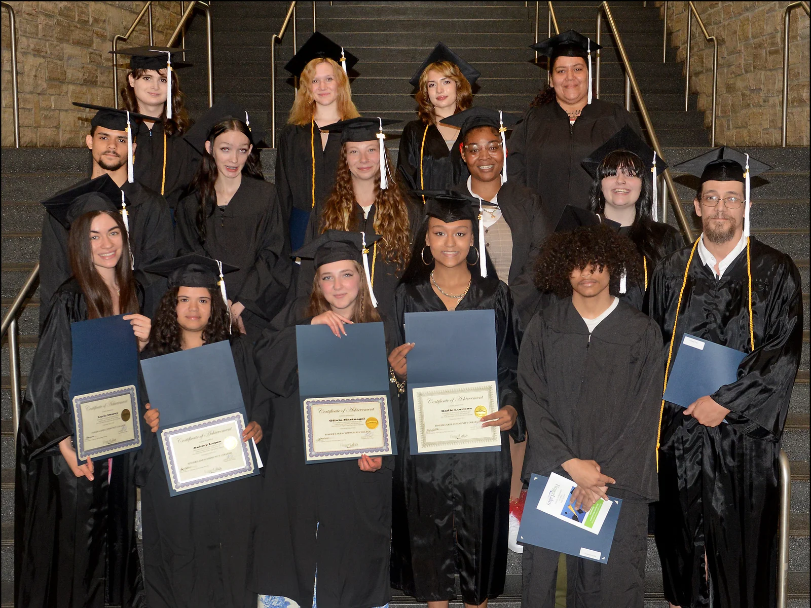 Posed photo of 15 students in black caps and gowns