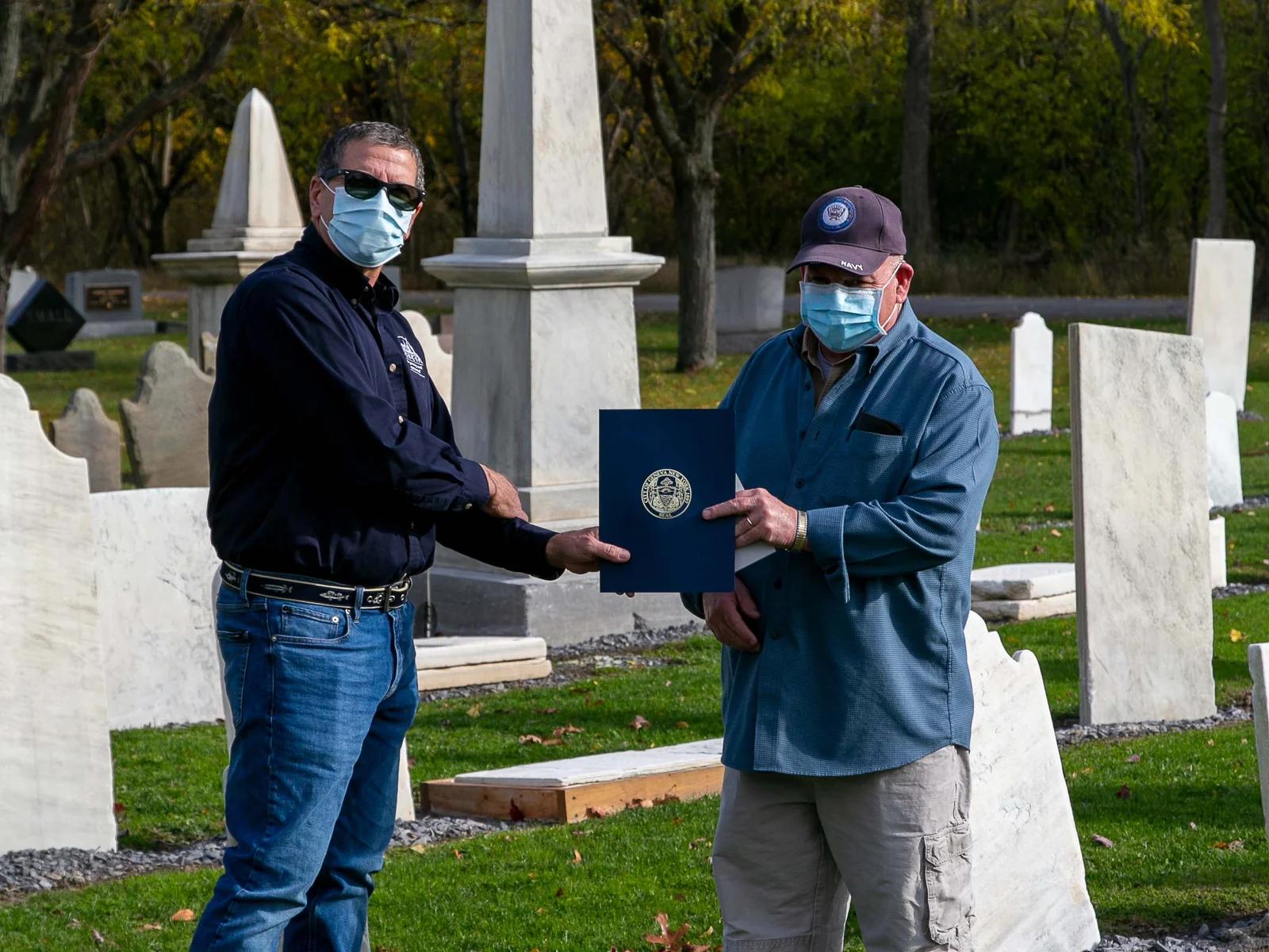 Two men standing in a cemetary holding a plaque