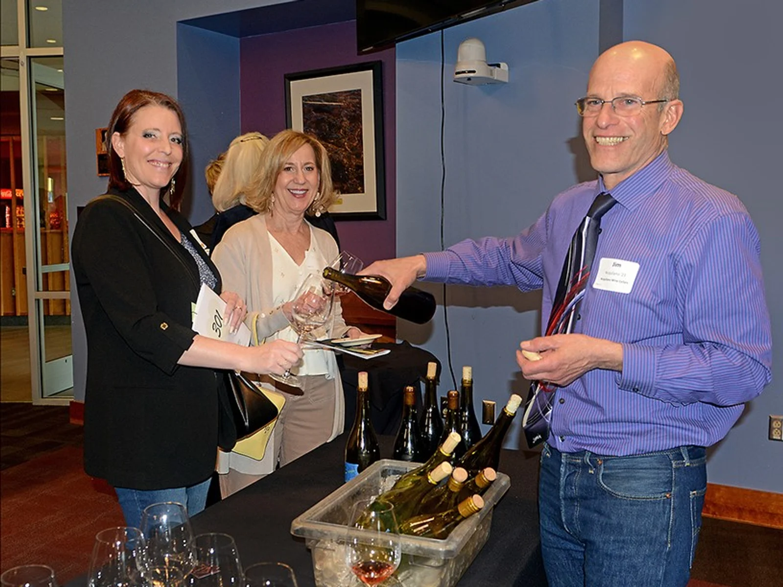 Man standing and pouring wine for 2 women on opposite side of table
