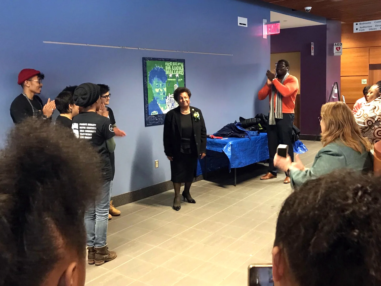 Woman standing in front of a small mural depicting her