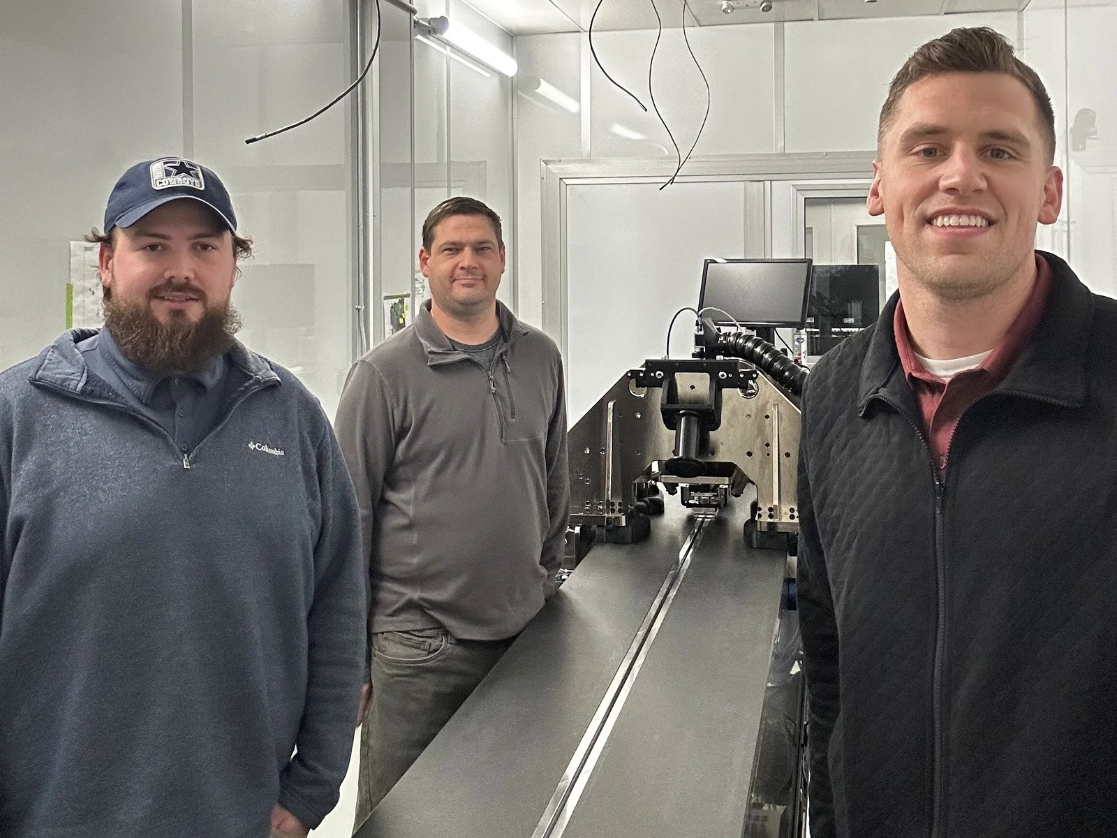 Three men standing next to a long metal table