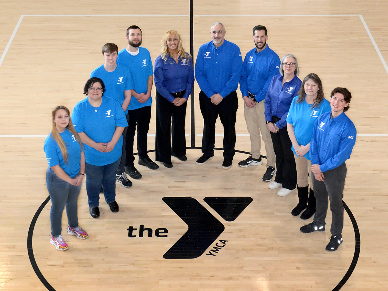 10 people standing in a semicircle around the YMCA logo painted on the gym floor