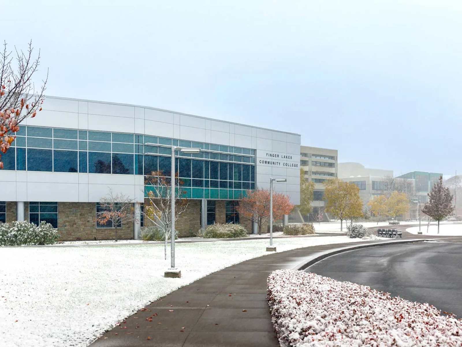 FLCC campus in the winter with snow falling onto trees with fall leaves.