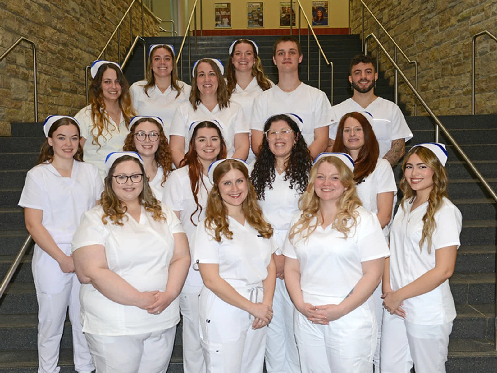 A group photo of 15 nursing graduates in white uniforms